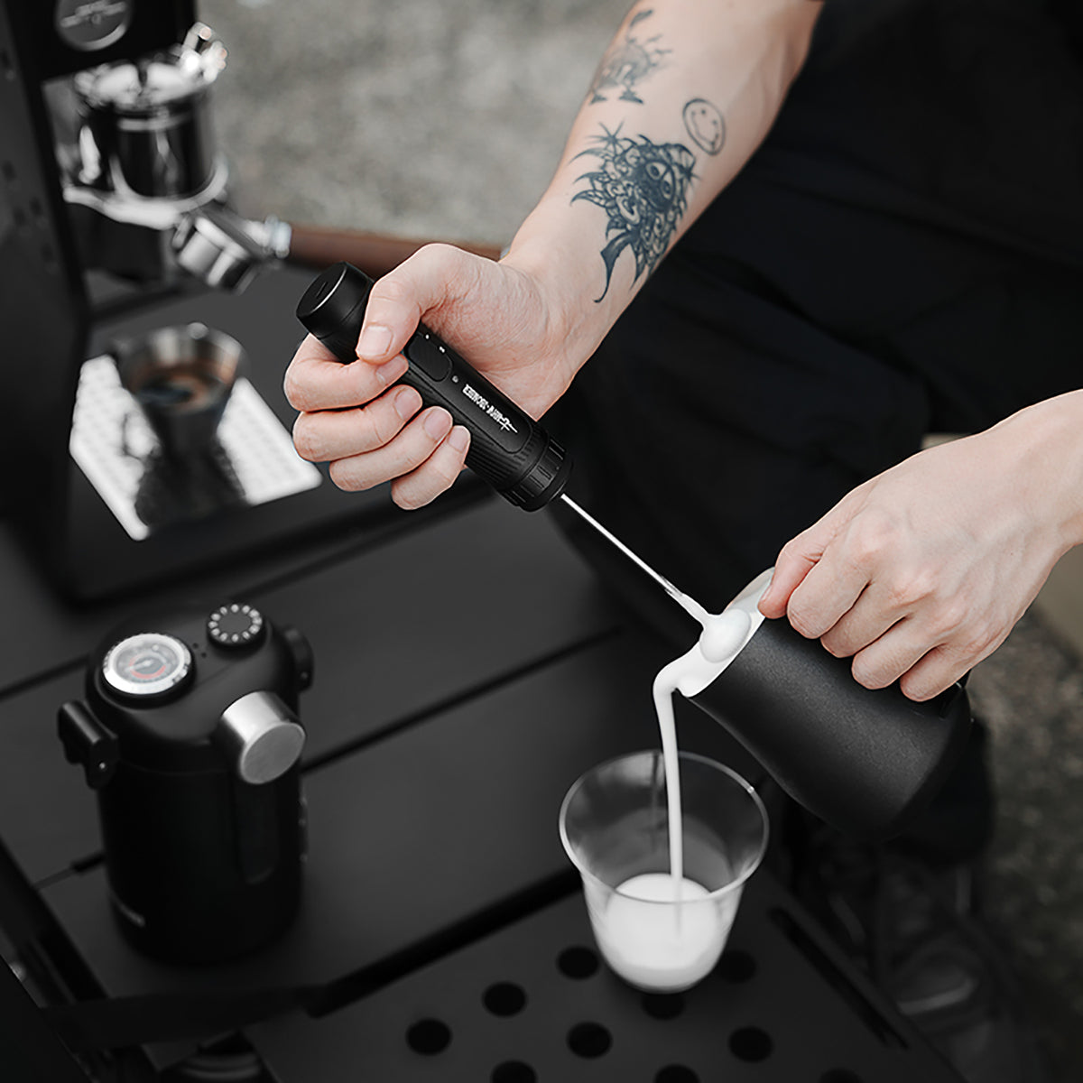 MHW-3BOMBER MF5893 black Magician frother held above milk being poured from a pitcher; pitcher and glass not included