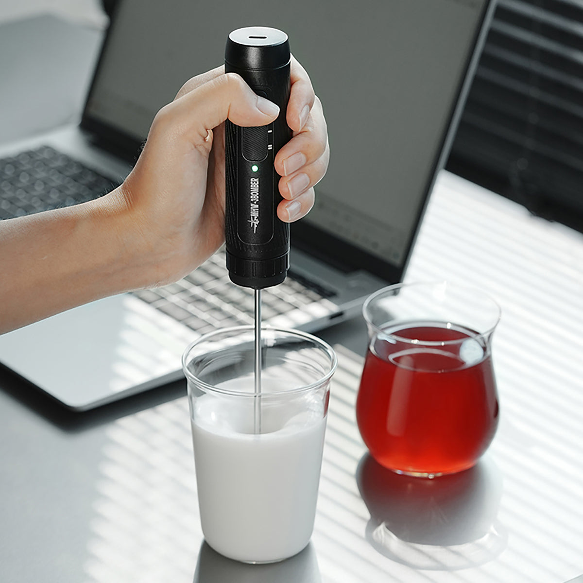MHW-3BOMBER MF5893 black Magician frother used in a beaker beside a red drink and laptop; beaker, drink and laptop not included