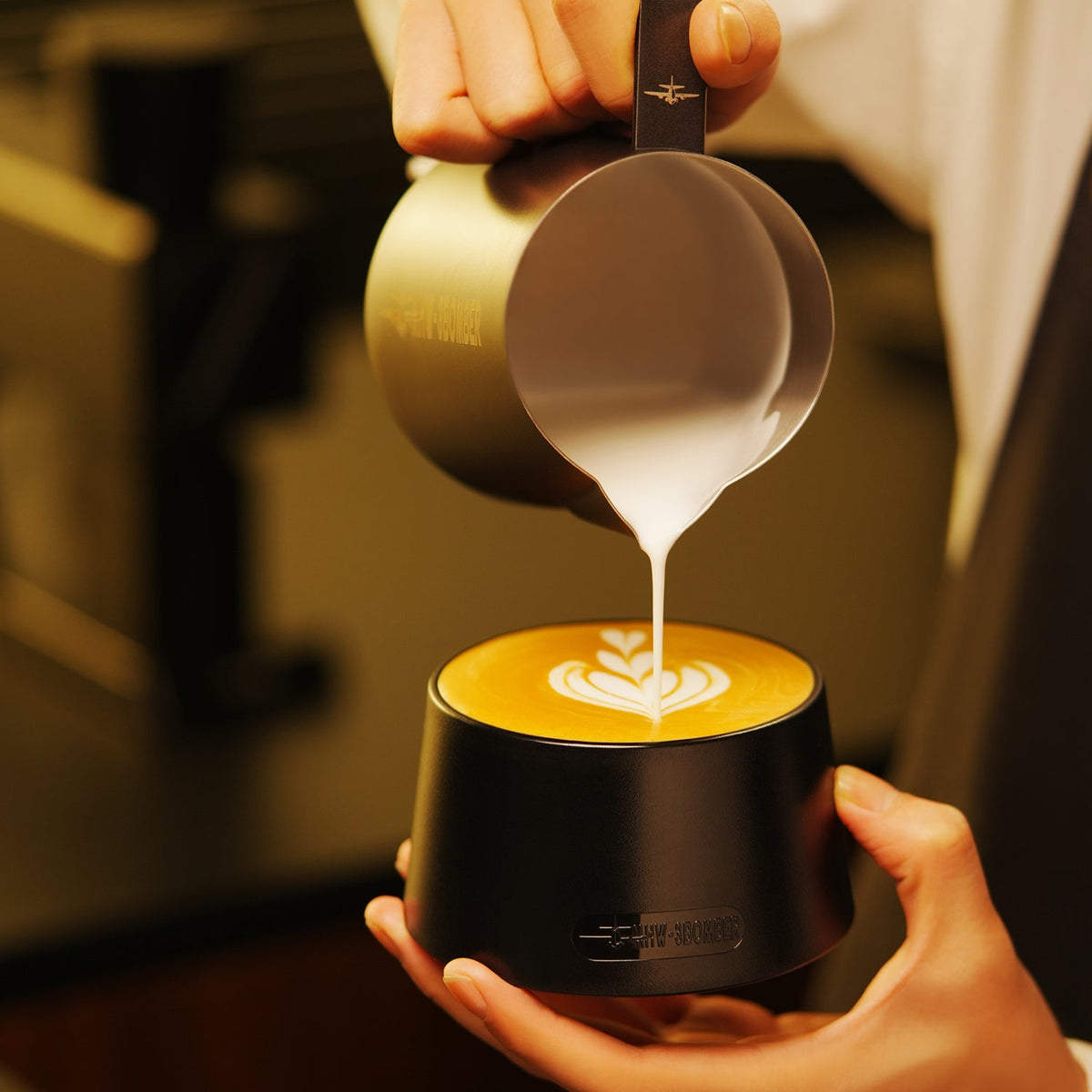 MHW-3BOMBER black cupping bowl held during latte pouring; milk pitcher and drinks are scene props, not included