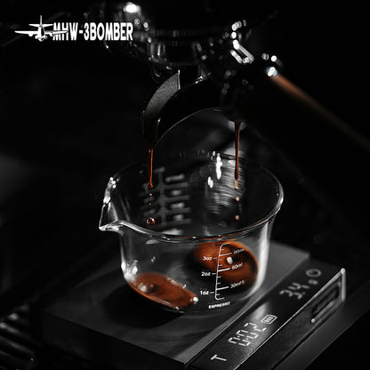 MHW-3BOMBER G5052 clear 120 ml single-spout measuring cup receiving espresso on a scale; machine and scale are separate props