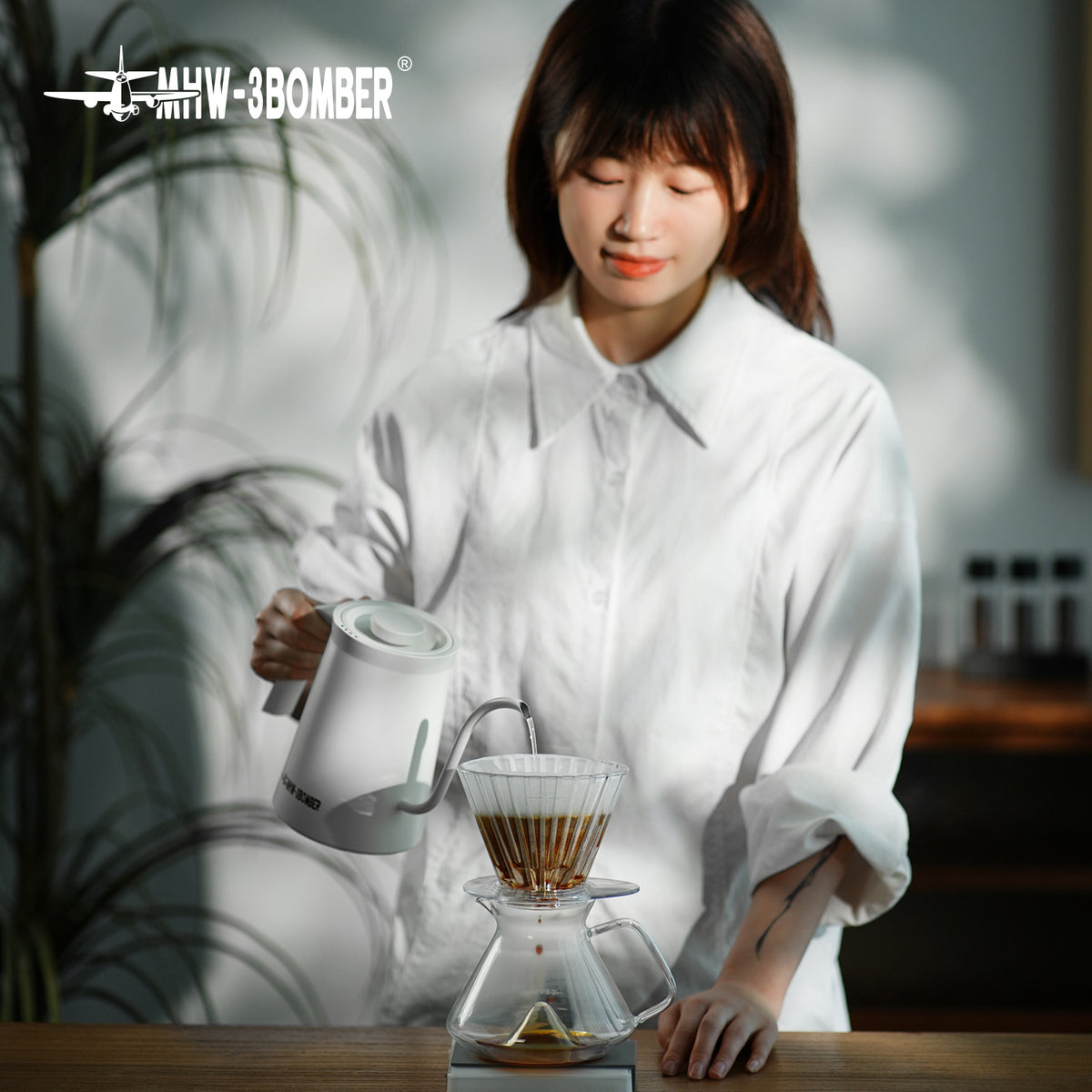 MHW-3BOMBER FC6605 — clear Oval dripper in a person-led pour-over setup; other tools are scene props