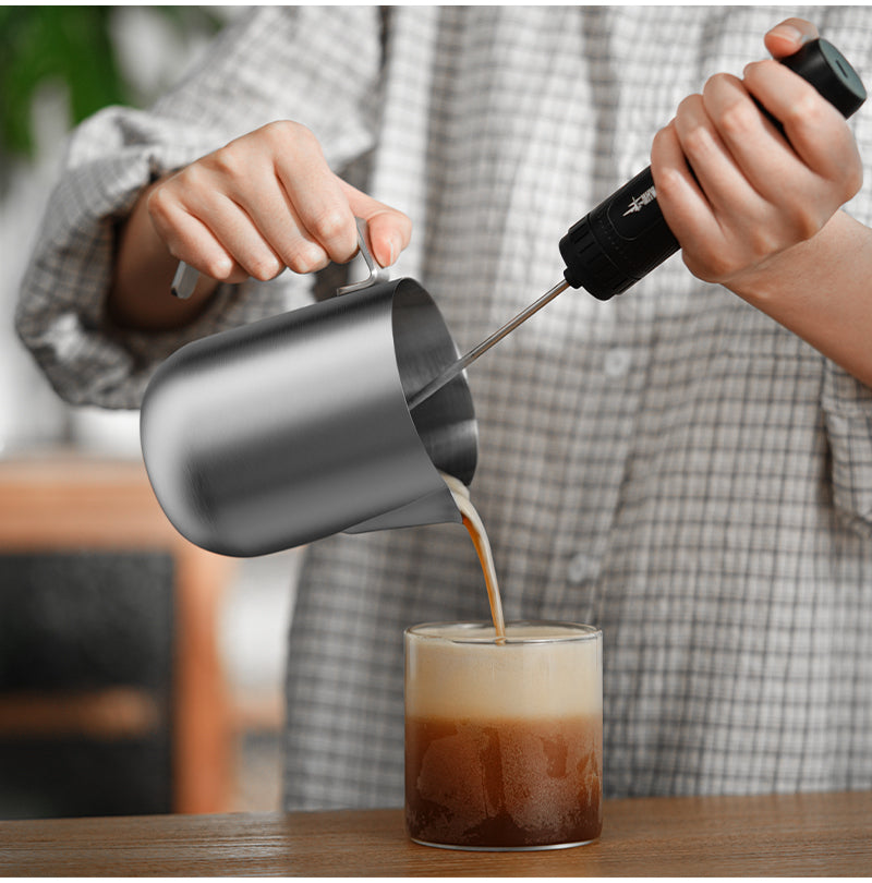 MHW-3BOMBER P5521 600 ml Silver Magician steaming pitcher pouring coffee into a glass while a separate frother is held over it; frother and glass not included