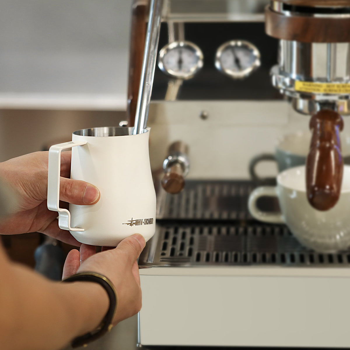 MHW-3BOMBER Turbo 450ml Off White milk pitcher held under a steam wand