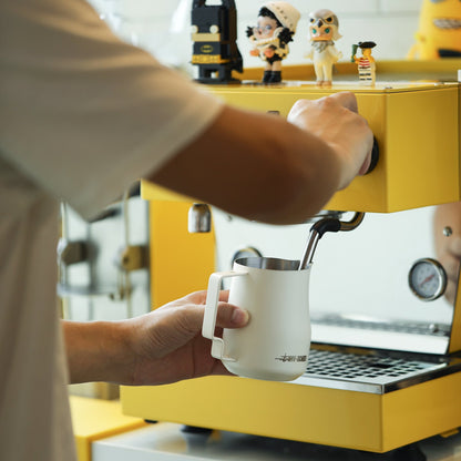 MHW-3BOMBER Turbo 450ml Off White milk pitcher at a yellow espresso machine
