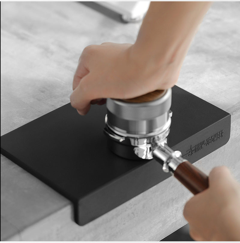 MHW-3BOMBER espresso tool held over the black A-style working surface