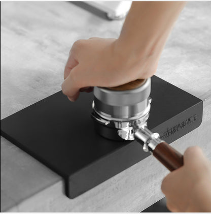 MHW-3BOMBER espresso tool held over the black A-style working surface