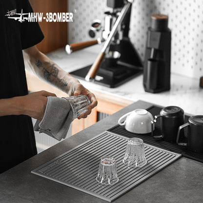 MHW-3BOMBER SP5325G Light Grey dish drying pad with ribbed surface at a coffee station; glasses and equipment not included.