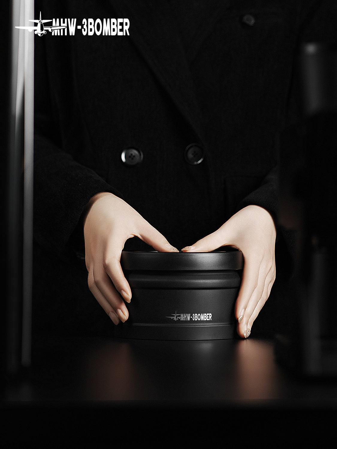 MHW-3BOMBER VC6033 black 750 ml coffee canister held with both hands on a dark counter.