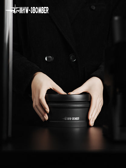 MHW-3BOMBER VC6033 black 750 ml coffee canister held with both hands on a dark counter.